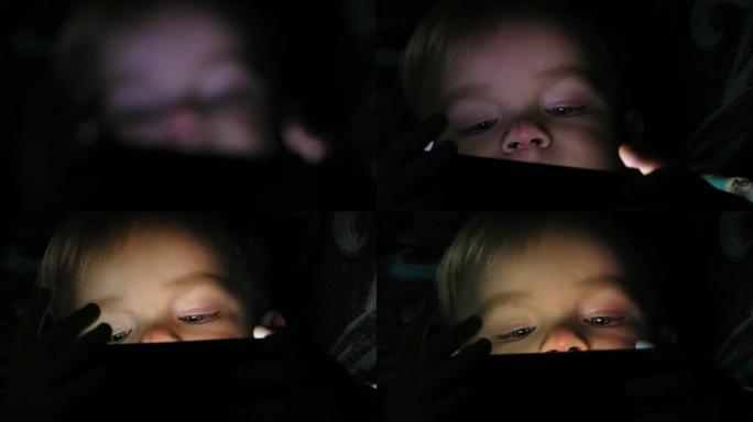 两年的男孩晚上在平板电脑上看动画片。