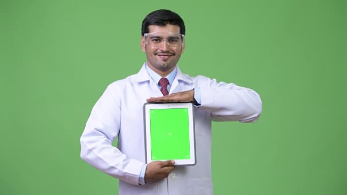 年轻英俊的波斯男子医生戴防护眼镜展示数码平板电脑