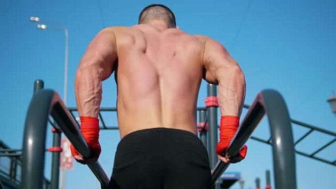 年轻肌肉发达的运动员在双杠处向上推-夏季户外锻炼-后视图