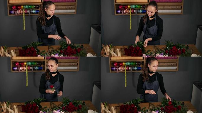 年轻的女花店在花店用美丽的红玫瑰安排现代花束。慢动作镜头