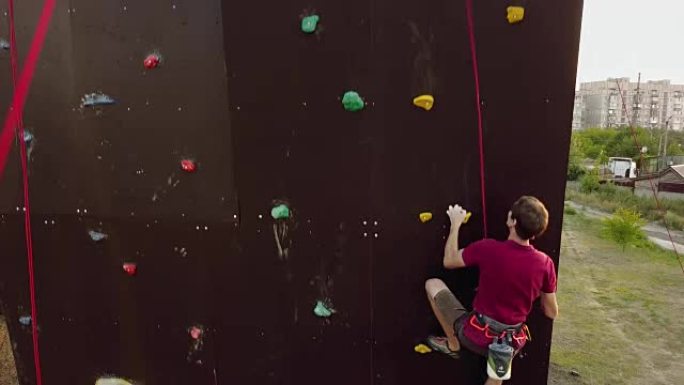 登山者的空中在户外的人造墙上运行速度攀岩轨道。年轻的快速运动员在比赛中爬上悬崖。系好安全带的人在抱石
