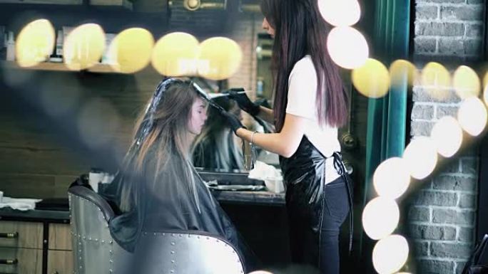 美发师用箔纸在女人的长发上涂上染发剂。年轻的时髦女孩坐在发廊的椅子上染头发。闪烁灯