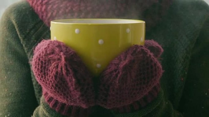 女人在冬天的早晨从黄色杯子里喝热茶或咖啡