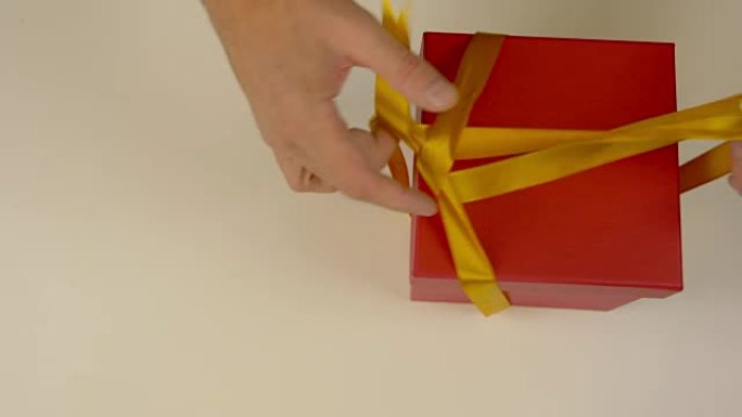 带金丝带的大未包装红色礼品盒。双手解开红色礼品盒上金色丝带的丝带。顶视图高角度。特写。