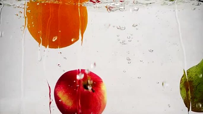 梨，苹果和橙子随气泡落入水中的慢动作视频。孤立的白色背景上的水果。