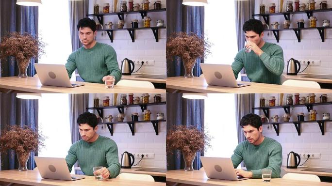 男子从玻璃杯中喝水并在笔记本电脑上工作