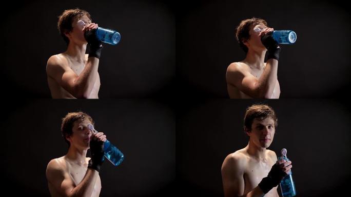 年轻的白人赤裸上身的拳击手从瓶子里喝水，休息，看着镜头，黑色背景50帧/秒