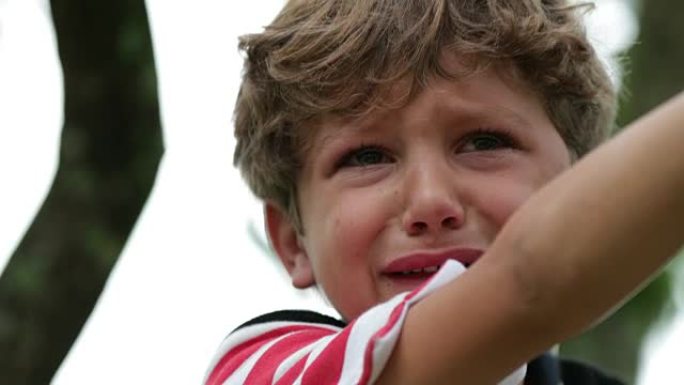 哭泣的孩子。现实生活中真实的坦率地抽泣着一个泪流满面的孩子在树顶上。痛苦的哭泣小男孩在4k中哭泣