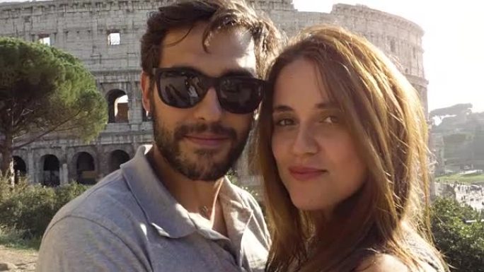 快乐的年轻夫妇游客在日落时在罗马斗兽场前拍摄自拍视频，微笑着享受摄像机的视点