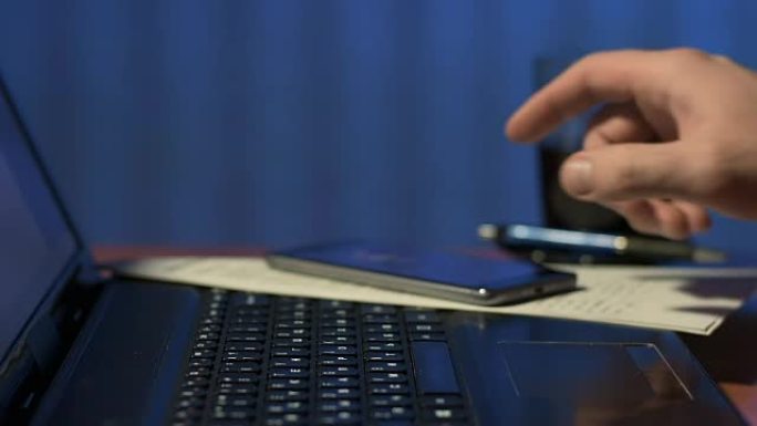 办公室男人的特写镜头在笔记本电脑的触摸屏上移动手指，在手机上接听来电