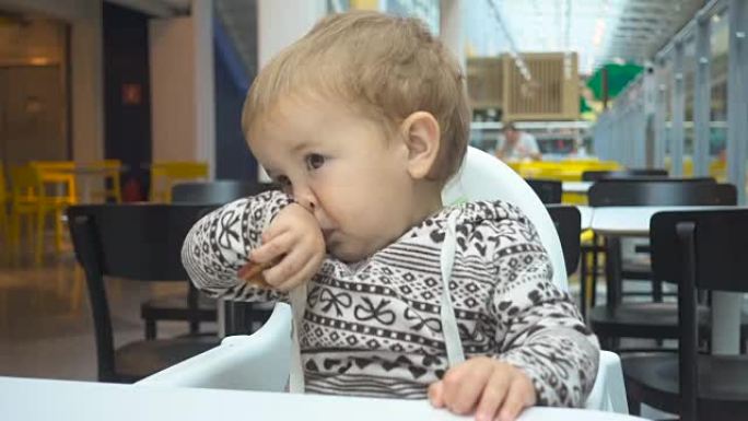 一岁的孩子在咖啡馆吃饭。男婴坐在咖啡馆的桌子旁，拿着蛋糕。