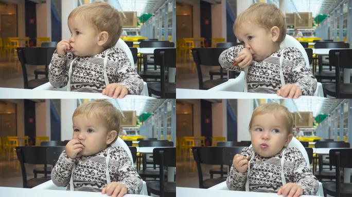一岁的孩子在咖啡馆吃饭。男婴坐在咖啡馆的桌子旁，拿着蛋糕。