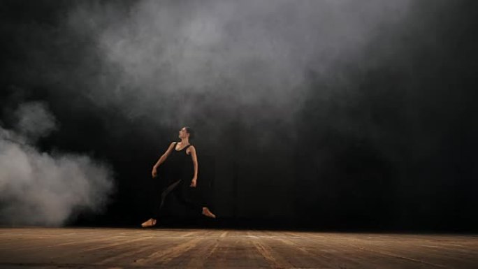 表演时，年轻美丽的女孩舞者在烟雾黑暗的舞台上跳得很高。穿着现代服装的芭蕾舞演员在现场性感地跳舞。史诗
