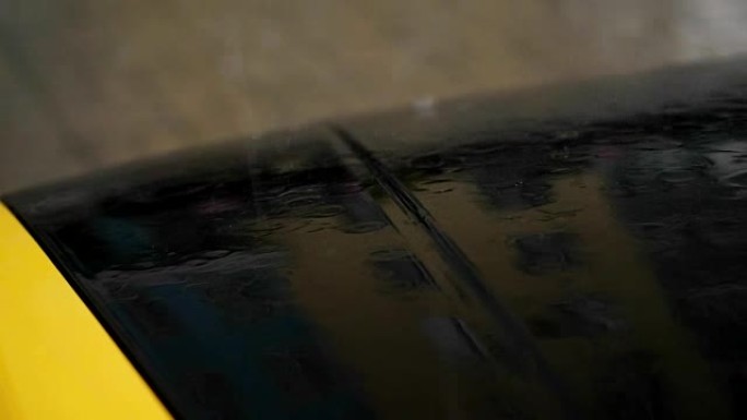 特写，有大雨，阵雨，沉重的水滴落下，在黑色和黄色的汽车引擎盖的潮湿表面上站在停车场。汽车在雨中变湿
