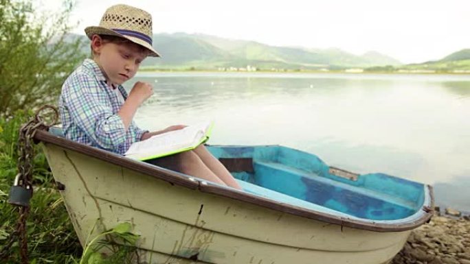 男孩坐在停泊在河岸的木船上看书