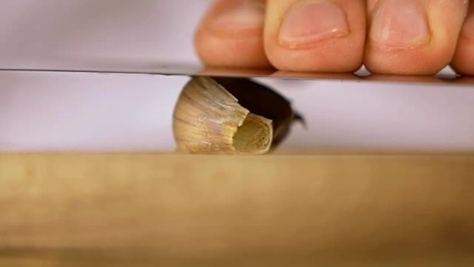 用刀片将一瓣大蒜压在木砧板上的特写
