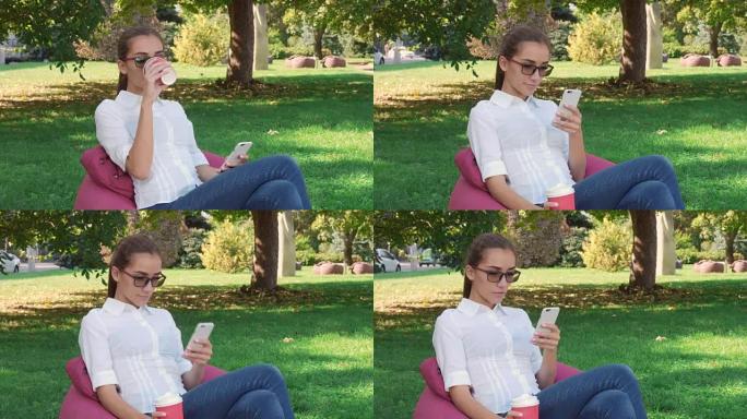 休闲年轻女子坐在城市公园喝咖啡，使用智能手机