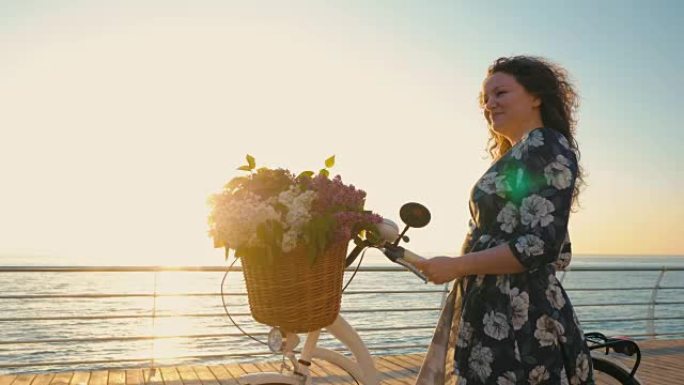 成年可爱的卷发女人穿着复古白色自行车连衣裙，在日出或日落时站在海边。假期旅行时间。浪漫的场景。女性生