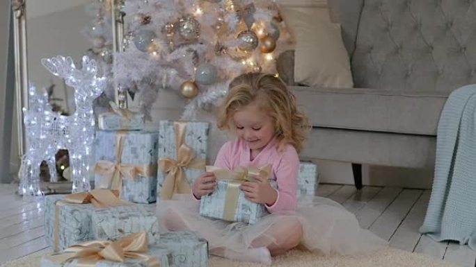 女孩坐在房子的地板上，带着圣诞礼物和花环。玩圣诞礼物的女孩