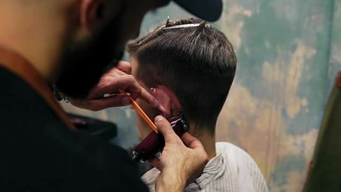 大胡子理发师在男人的耳朵后面使用电动修剪器创建一条直线。年轻英俊的白人男子在一家现代理发店理发。慢动