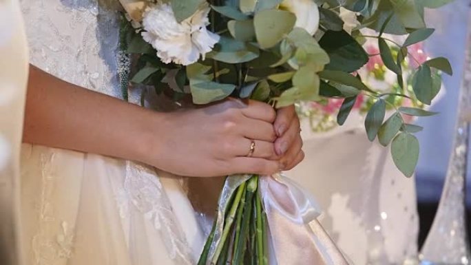 穿着白色婚纱的年轻新娘手中的美丽新娘花束。关闭大束新鲜的白玫瑰和郁金香花在女性手中。手持鲜花的匿名新
