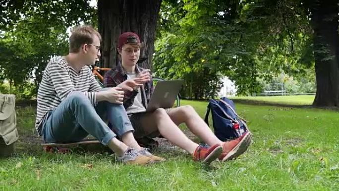 在温暖的天气和良好的天气下，两个有创造力的家伙在户外使用笔记本电脑在城市公园的草坪上讨论一个新项目
