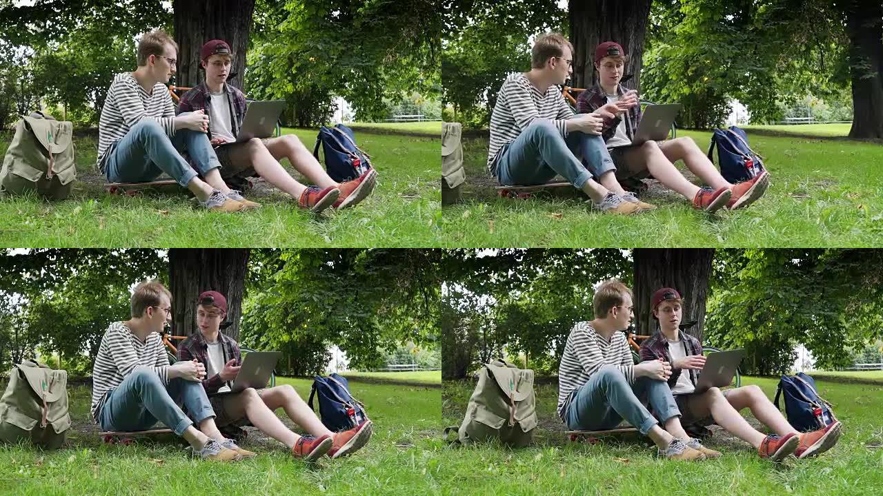在温暖的天气和良好的天气下，两个有创造力的家伙在户外使用笔记本电脑在城市公园的草坪上讨论一个新项目