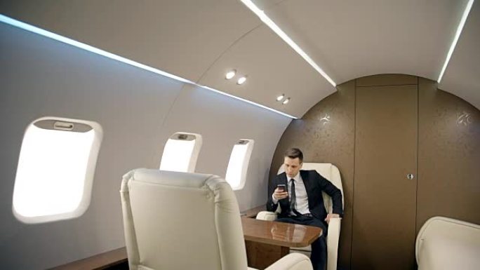 年轻成功的商人坐在私人飞机上使用智能手机