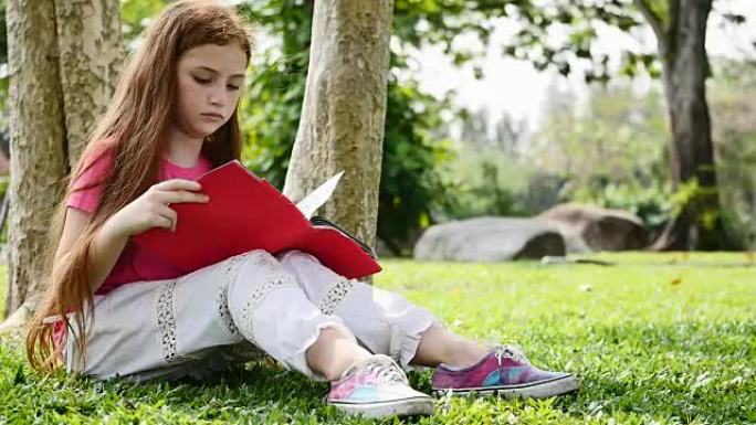 美丽的女孩坐在公园的绿草地上看书