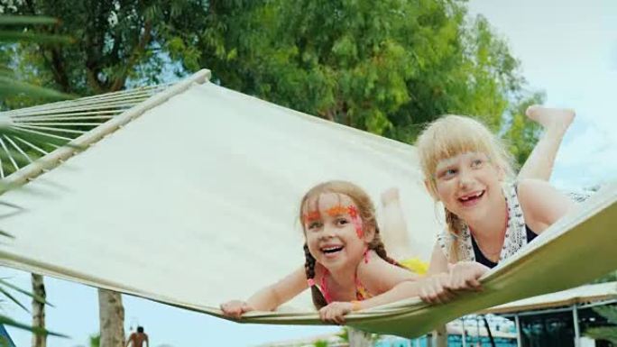 脸上充满水色的小孩子在酒店美丽的绿色林间空地上的白布吊床上快乐地滑冰