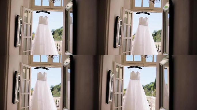 白色连衣裙挂在露台门口的专用衣架上。丝绸或雪纺面料制成的轻便夏季礼服在阳光明媚的早晨阳台上等待新娘。
