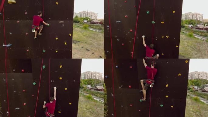 登山者的空中在户外的人造墙上运行速度攀岩轨道。年轻的快速运动员在比赛中爬上悬崖。系好安全带的人在抱石