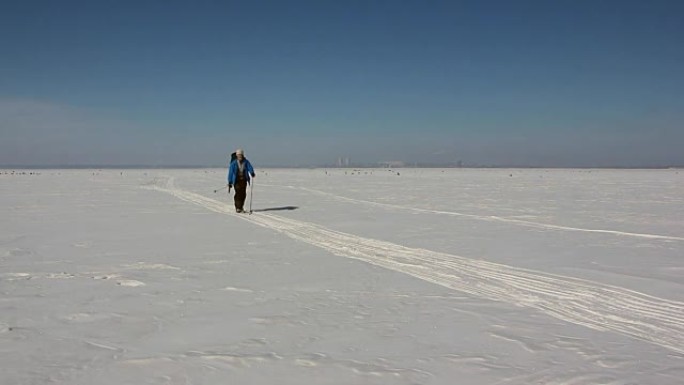 穿着蓝色夹克和背包的男人正在冰冻的河流的冰上滑雪