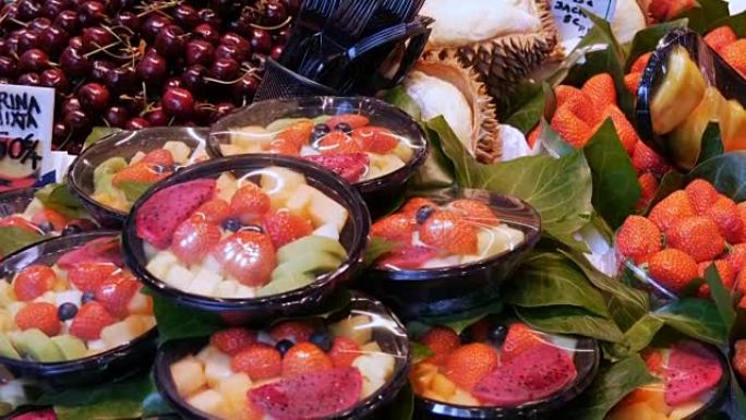 在西班牙巴塞罗那水果市场柜台的塑料板中混合不同的草莓水果芒果猕猴桃和其他