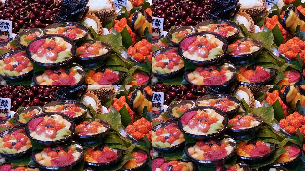 在西班牙巴塞罗那水果市场柜台的塑料板中混合不同的草莓水果芒果猕猴桃和其他