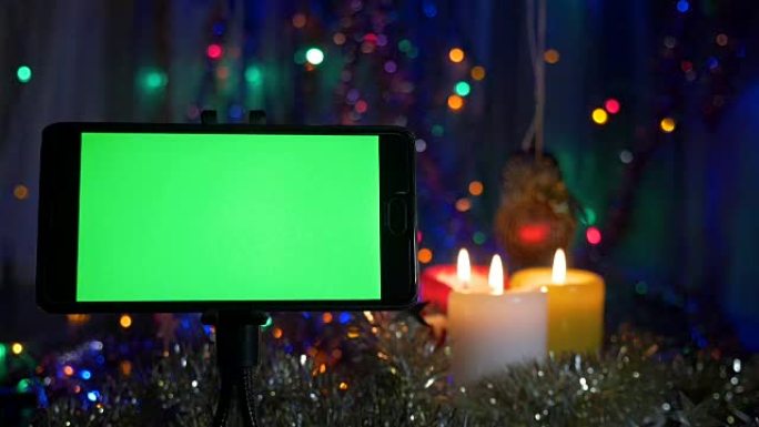 绿屏智能手机。在新年的背景上，闪烁的花环，燃烧的蜡烛。