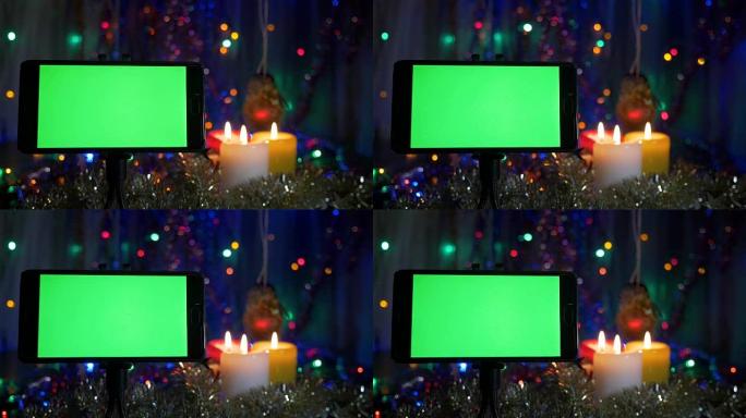 绿屏智能手机。在新年的背景上，闪烁的花环，燃烧的蜡烛。