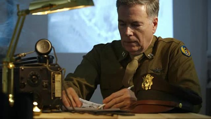 第二次世界大战的陆军航空兵上尉坐在他的办公桌旁看侦察照片