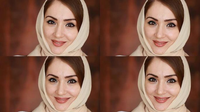 一位年轻而神秘的阿拉伯妇女的特写肖像戴着一条被称为头巾的轻便头巾，微笑着看着相机。深棕色背景上美丽的