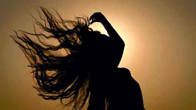 匿名女人在天空日落灯光的背景上颤抖着头发