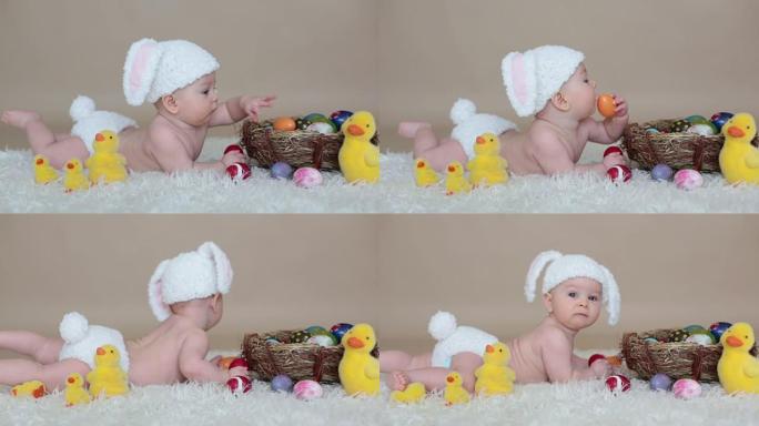 可爱的蹒跚学步的小男孩，玩五颜六色的复活节彩蛋和小装饰鸭子，孤立的镜头，米色背景