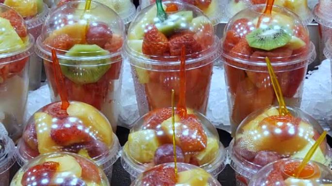 新鲜的新鲜包装在塑料玻璃混合物中，混合了西瓜，猕猴桃，梨，苹果，芒果，石榴，草莓的水果，叉子紧贴在其