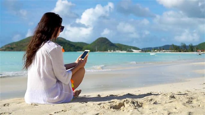 在热带海滩度假期间，拥有智能手机的年轻女子。加勒比海岛上海滩上带着手机的漂亮女孩。慢动作