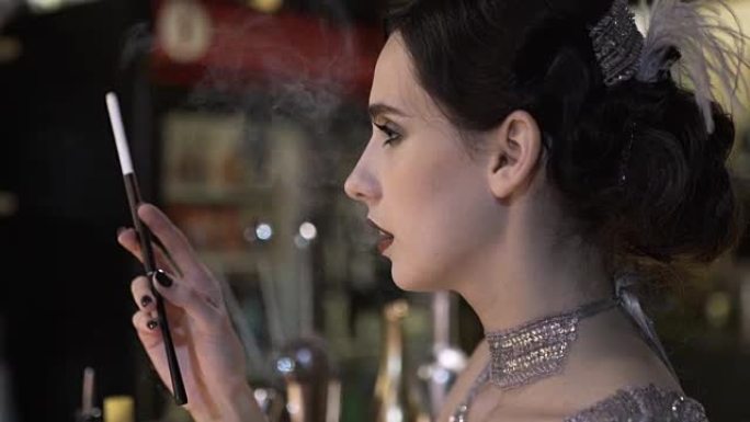 酒吧里一个年轻迷人的女人穿着20世纪20年代风格的香烟的肖像。化妆漂亮的模特