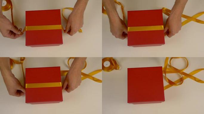 准备礼品包装。一盒红色的纸板。男士手测量金缎丝带来装饰礼品盒。俯视图特写。黄色胶带。