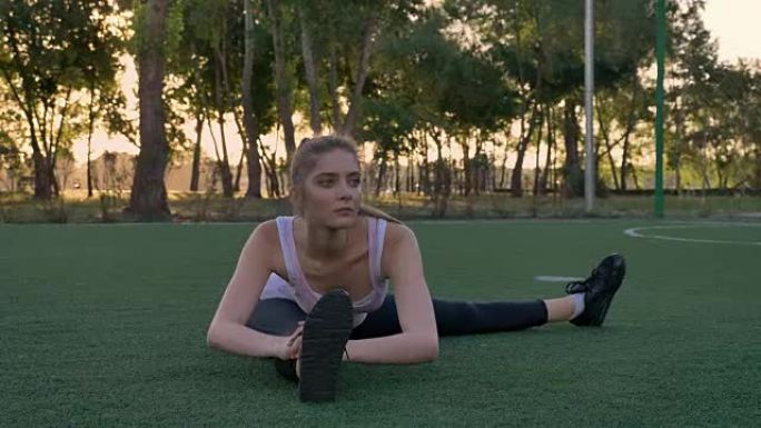 年轻漂亮的女人在公园的足球场上伸展，晨练，健身模型锻炼
