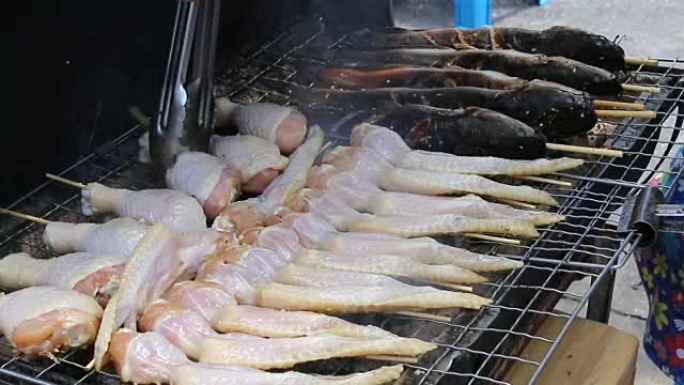 商人用火在火炉上烤新鲜鸡翅，在火上冒烟。街上的泰国菜，视频片段1920x2080。手工烹饪概念。