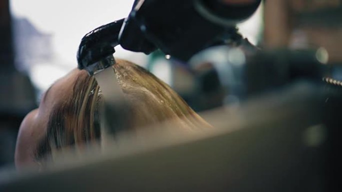 穿着黑色手套的理发师在美容院洗金发女人的头发，特写镜头后视图