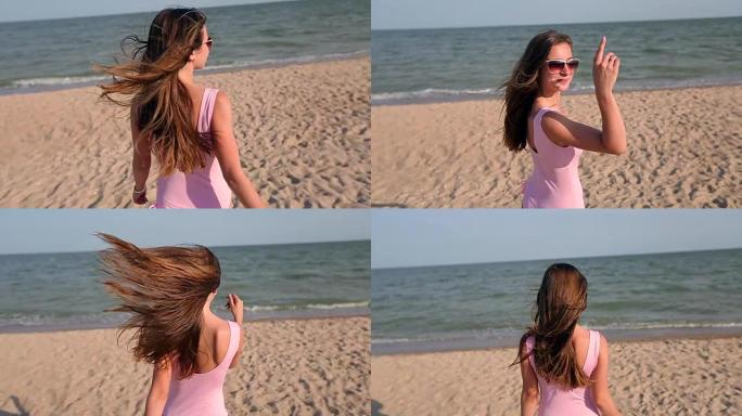女人在海滩上漫步到海水，转身并邀请她去度假旅行。穿着粉色泳衣的热带白色沙滩上身材苗条火辣的女士走向海