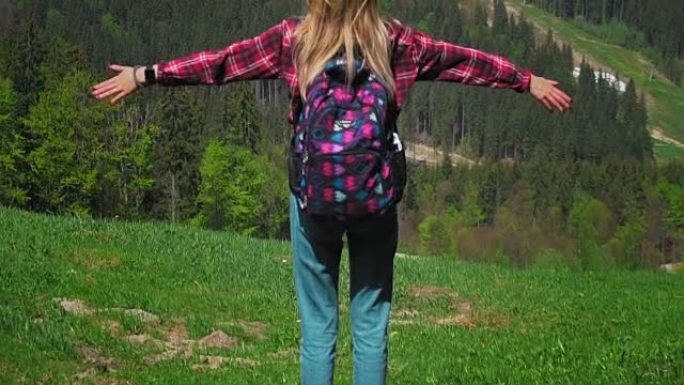 一位年轻的白人妇女背着背包和太阳镜站在山顶上，举起双手。个人成长，克服业务困难，个人动机，自由和自我